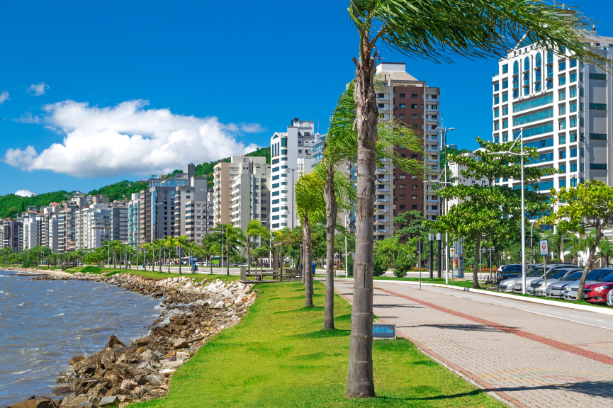 Coastal residential neighborhood in Florianópolis, Brazil, showcasing modern apartment buildings, waterfront promenades, palm trees, and a high-quality urban lifestyle.